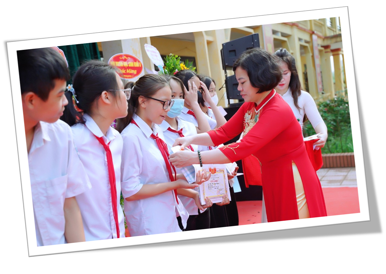 A person in a red dress handing a piece of paper to a group of children  Description automatically generated
